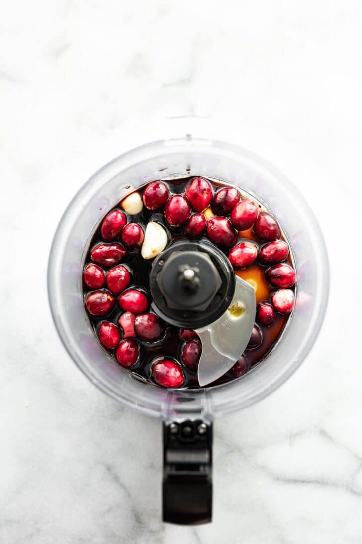 overhead image of a food processor full of cranberries, garlic, honey, etc. to make cranberry marinade