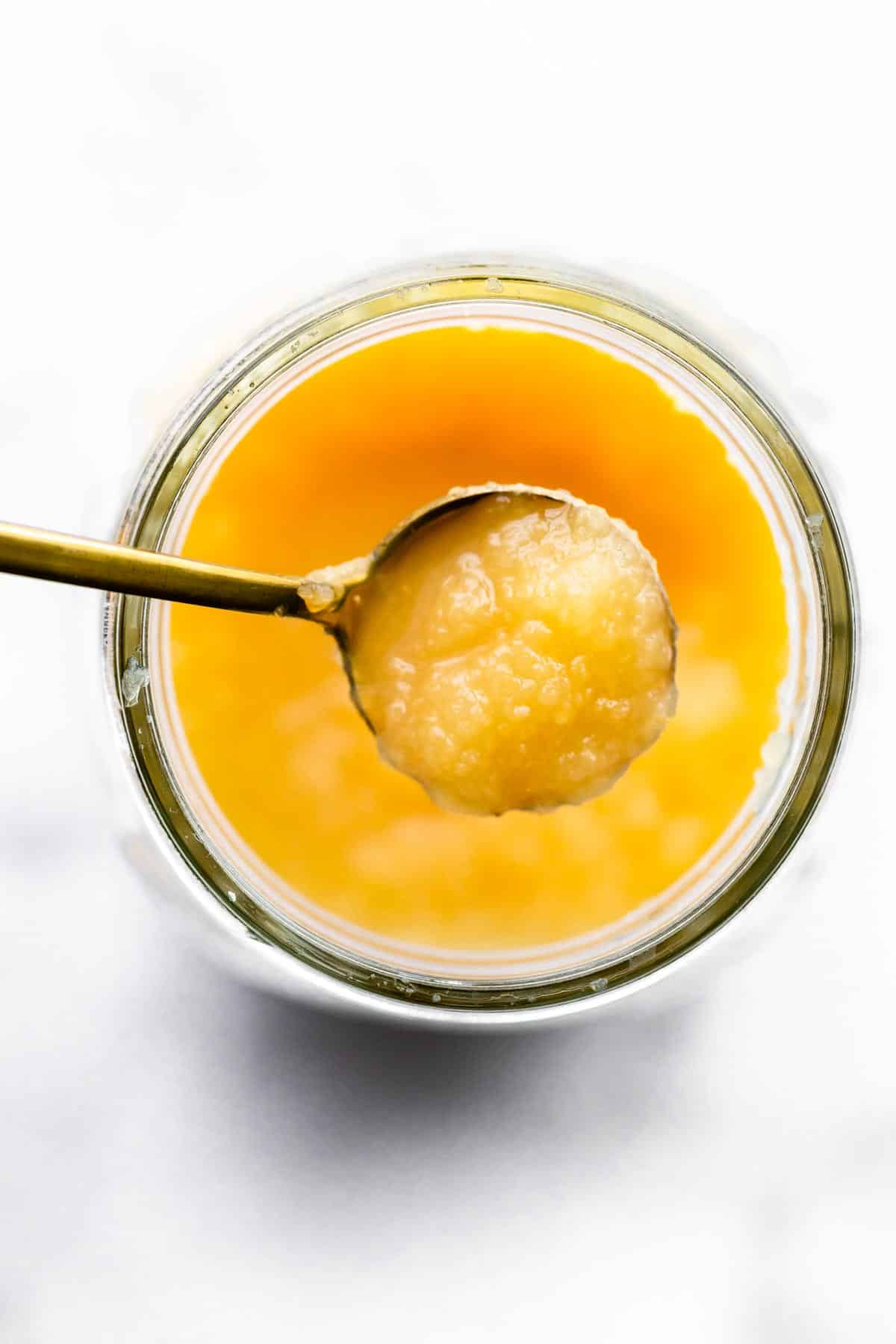 overhead image of a spoon full of applesauce over a jar of applesauce
