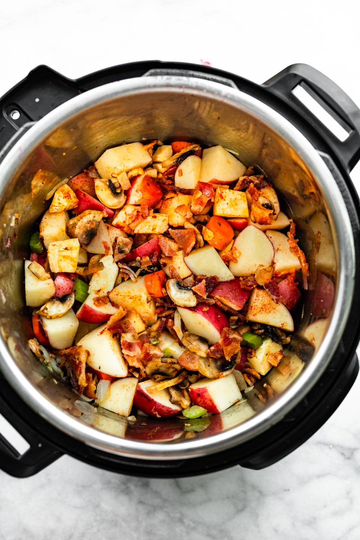 Potatoes, onions, celery, carrots, parsnips, and mushrooms in an instapot cooking.