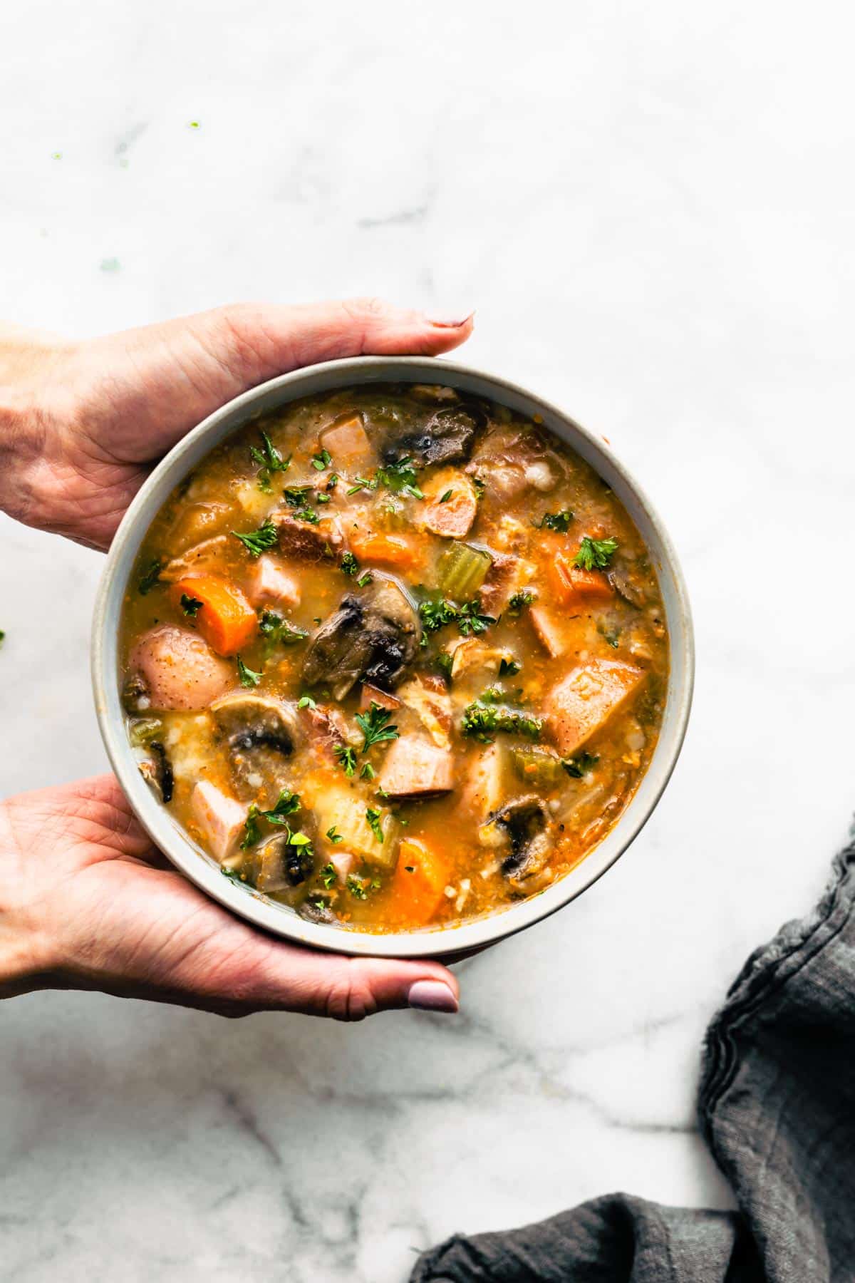 Hands holding a bowl of slow cooker vegetable soup with bacon