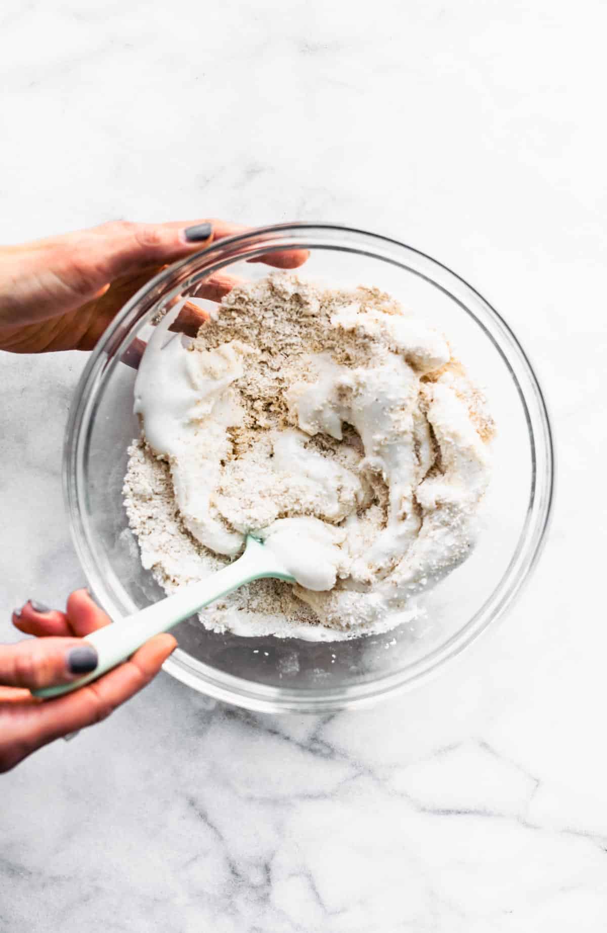 two hands holding a bowl of vegan mocha coconut macaroon batter, mixing it together