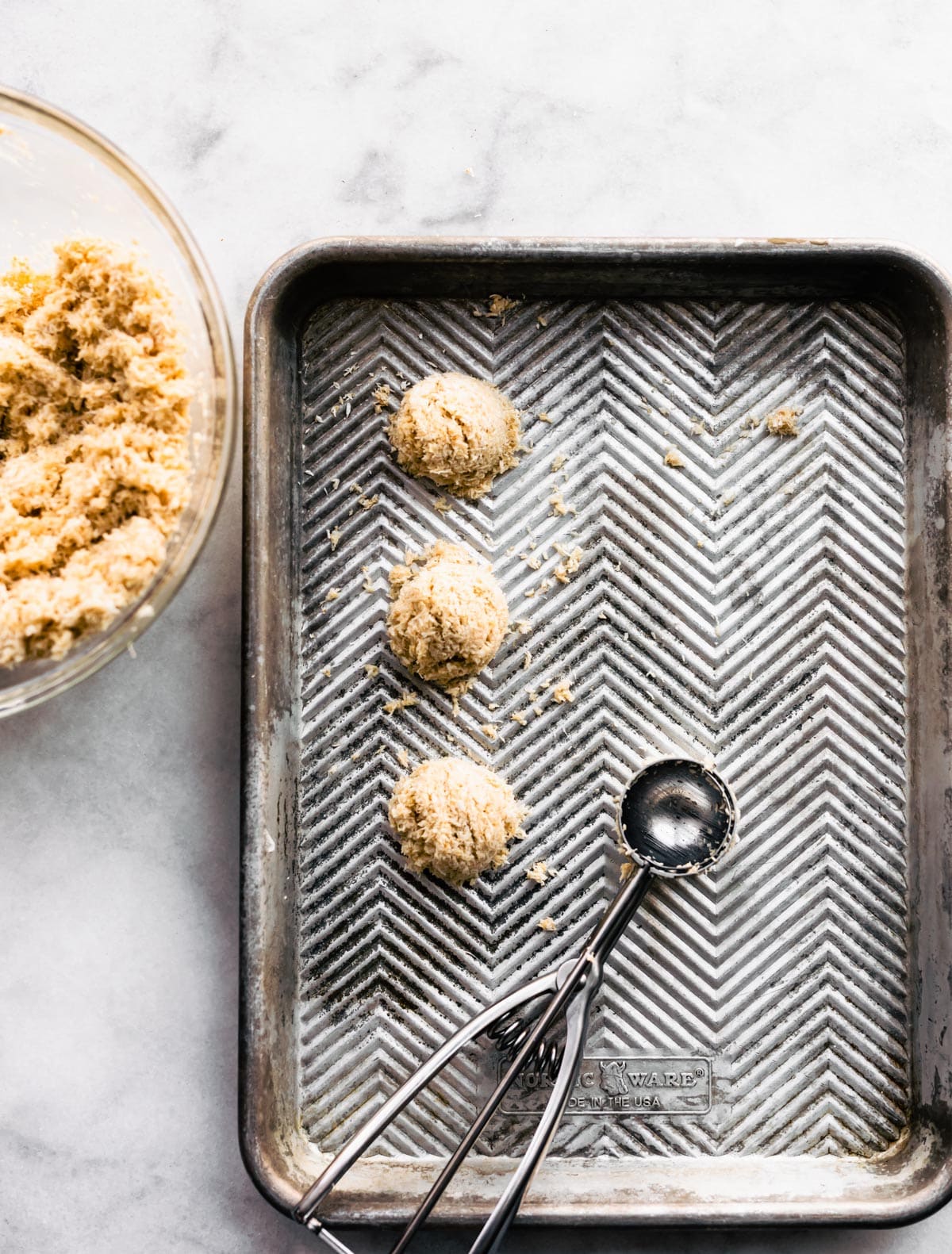 a baking sheet with three mounds of mocha coconut macaroons and a cookie scoop