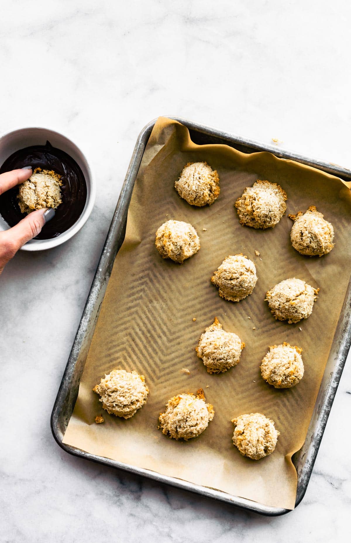 a sheet pan full of vegan gluten free mocha coconut macaroons with a hand dipping one into dark chocolate