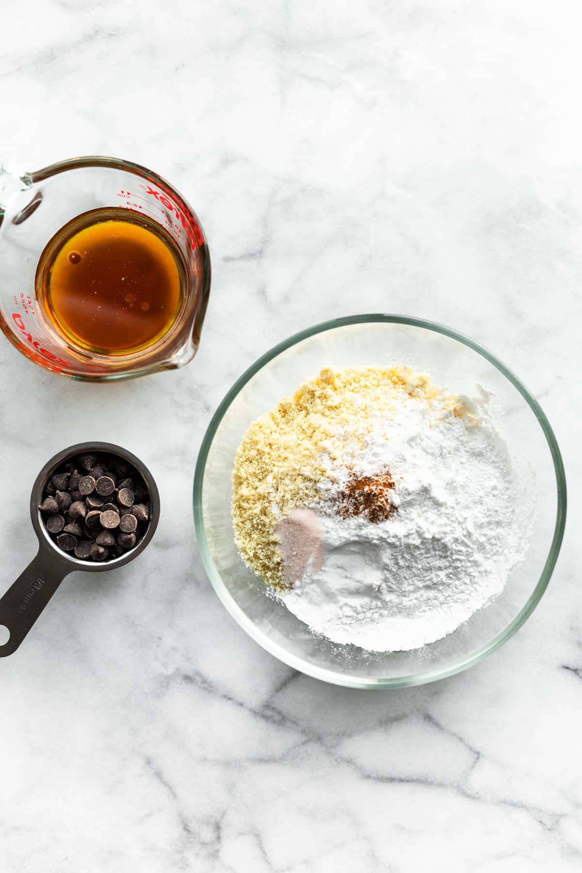 overhead image of a measuring cup of maple syrup, a bowl of dry ingredients, and ⅓ cup of chocolate chips