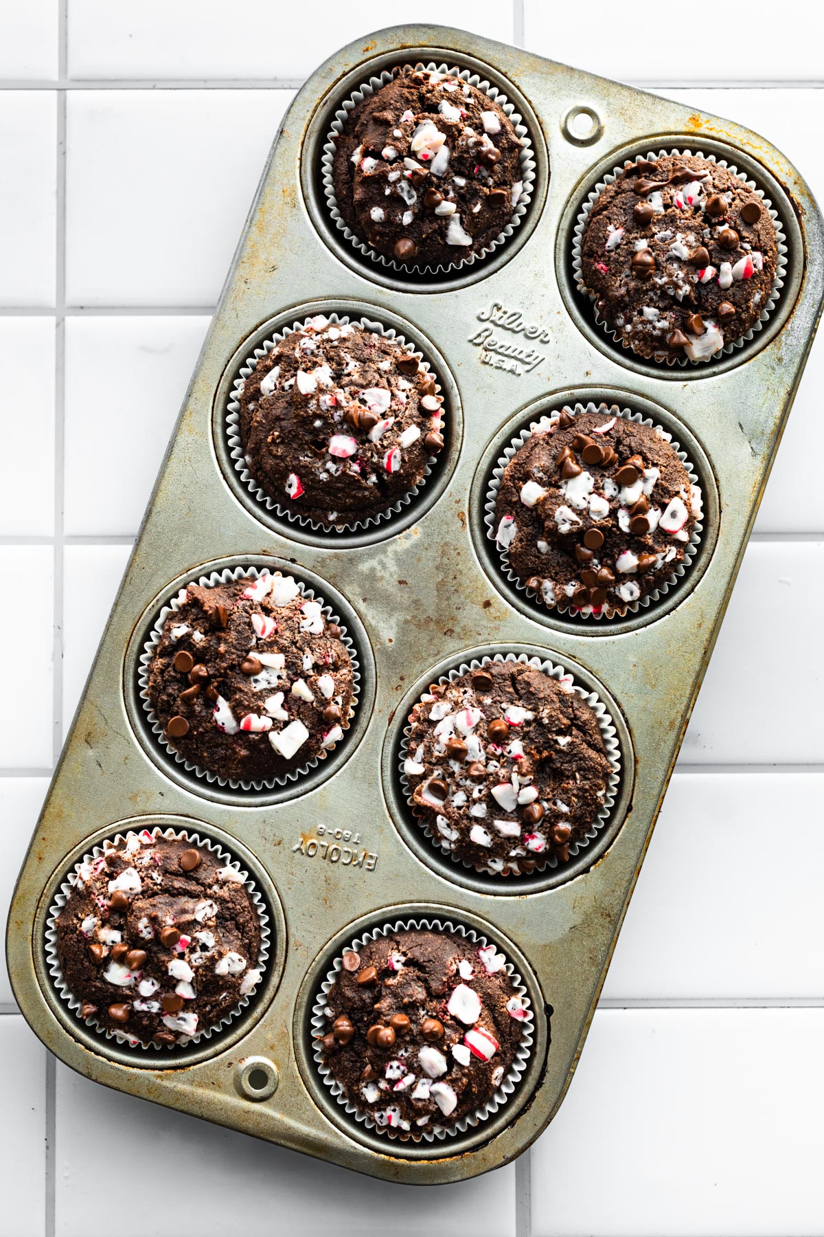 A pan of baked gluten free chocolate peppermint muffins topped with crushed candies.