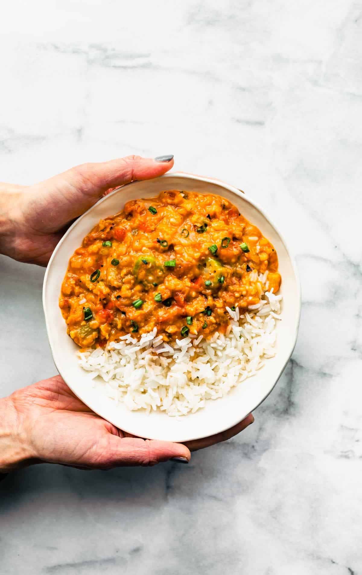 Hands holding a bowl of Instant Pot Gumbo over rice.