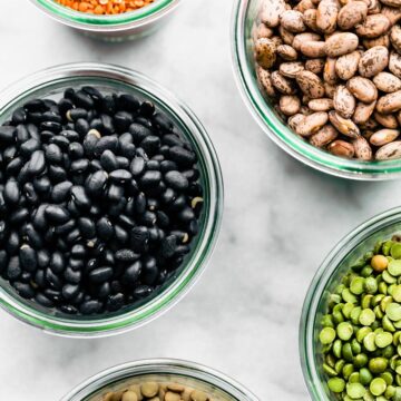 overhead shot of dried beans, legumes, lentils, and split peas in clear bowls