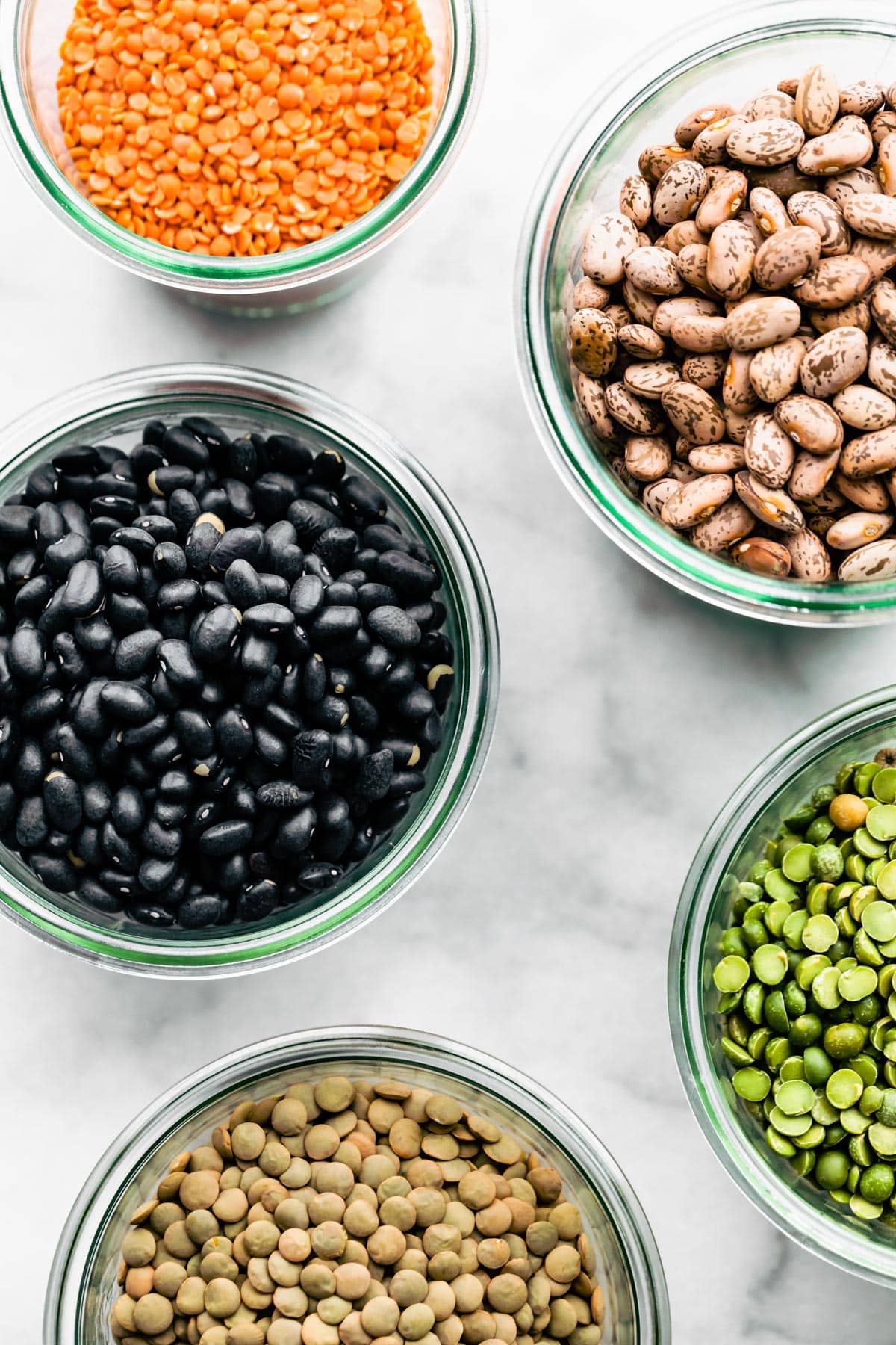 Overhead shot of lentils, kidney beans, black beans and split peas all in their own glass jars.