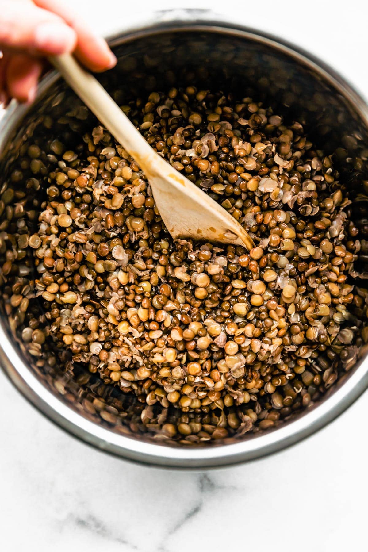 Brown lentils being stirred in a pot with a wooden spoon.