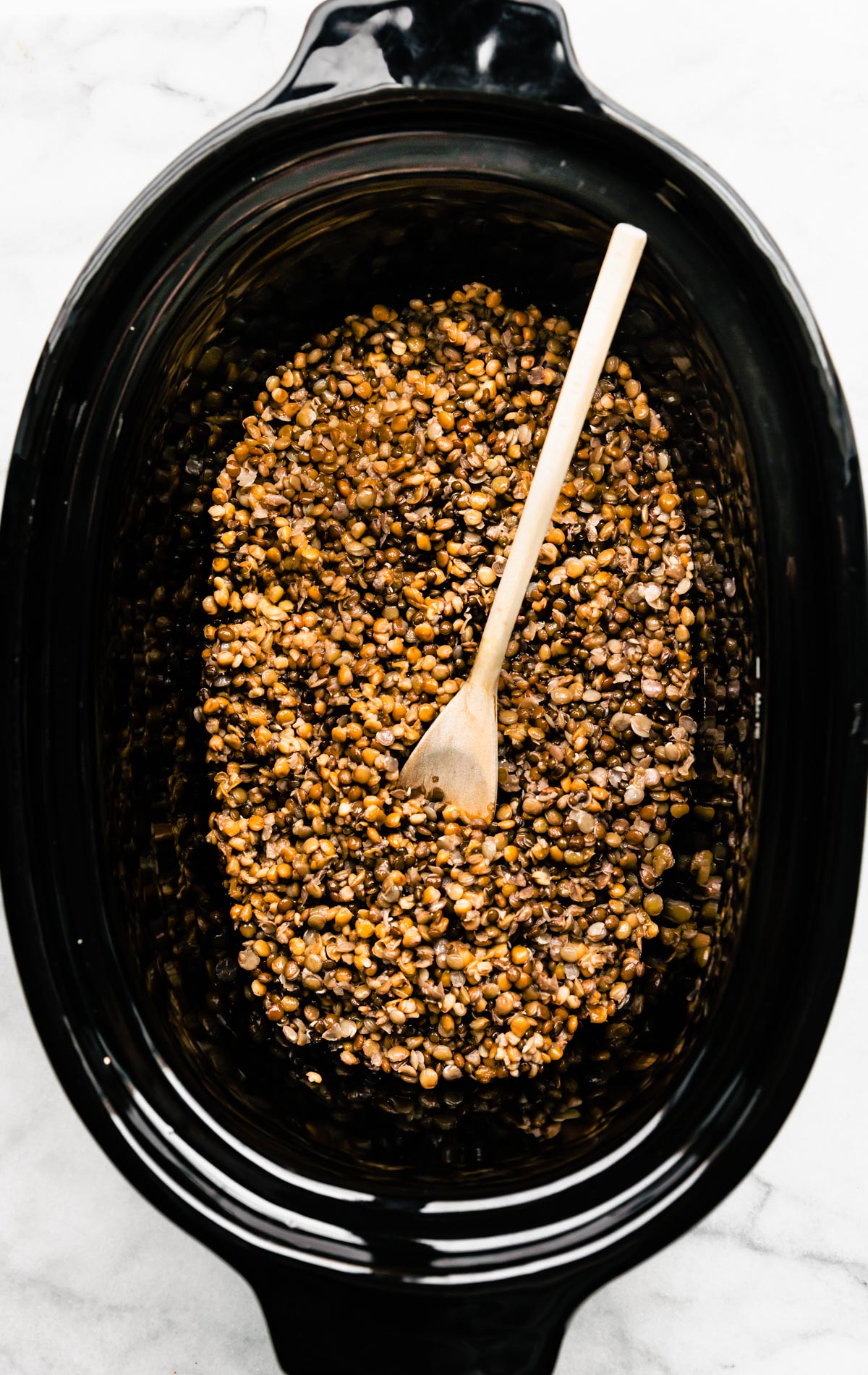 Brown Lentils in a slow cooker with a wooden spoon.