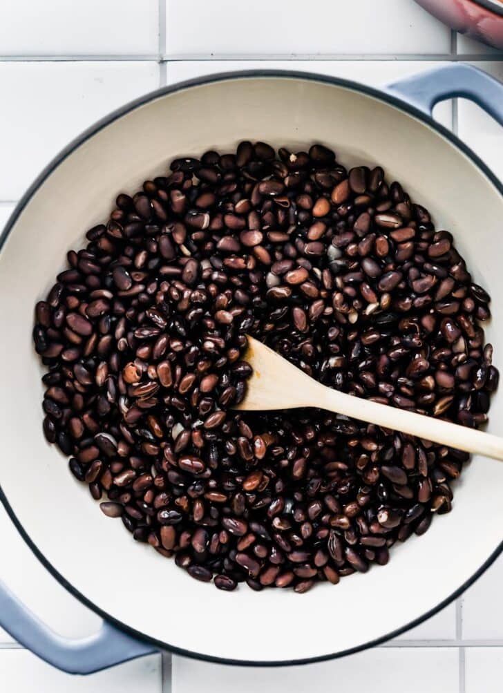Overhead shot of Black Beans being stirred in a pot by a wooden spoon.