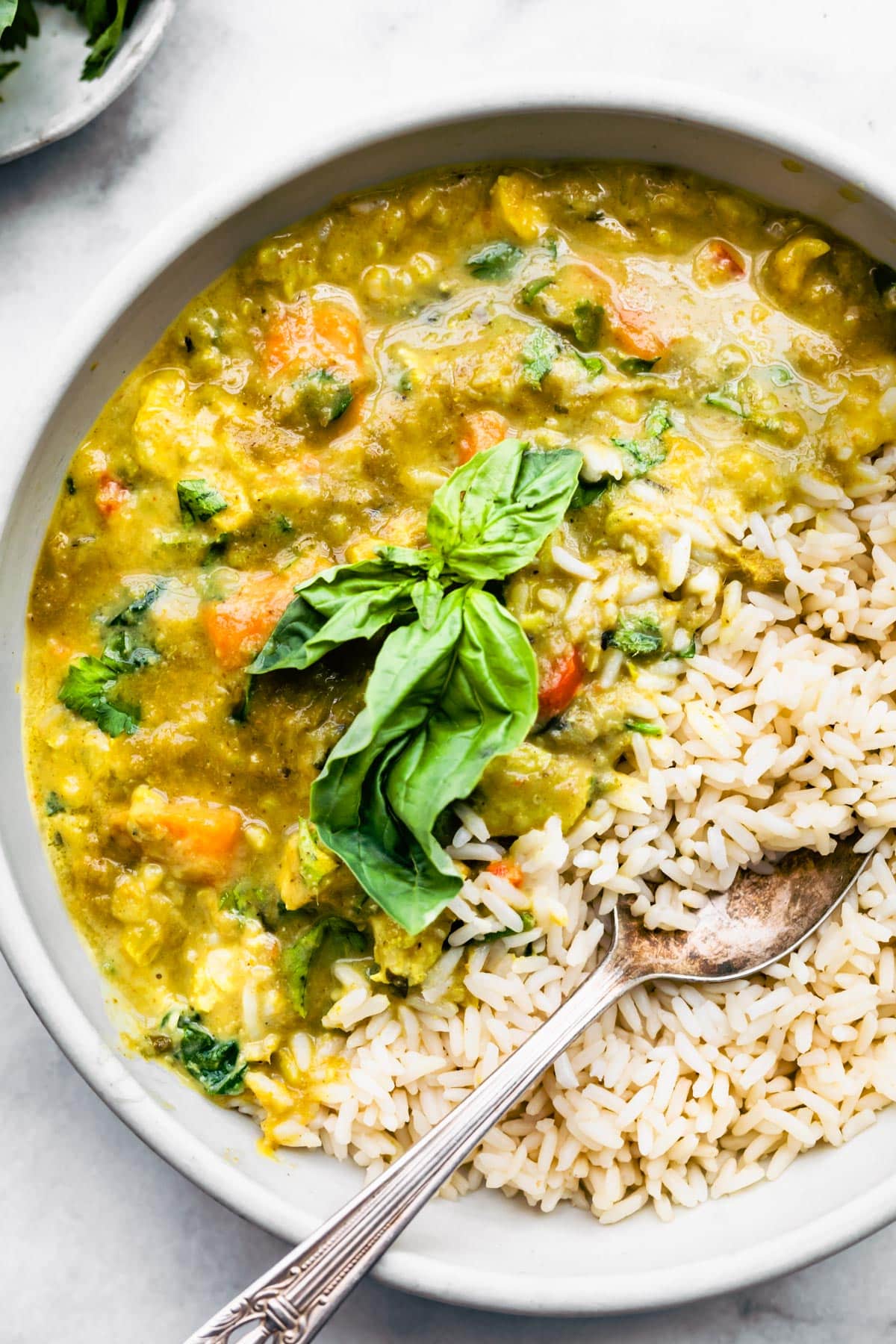 Close up over headshot of Chicken Green Curry and rice splitting a bowl and topped with greens