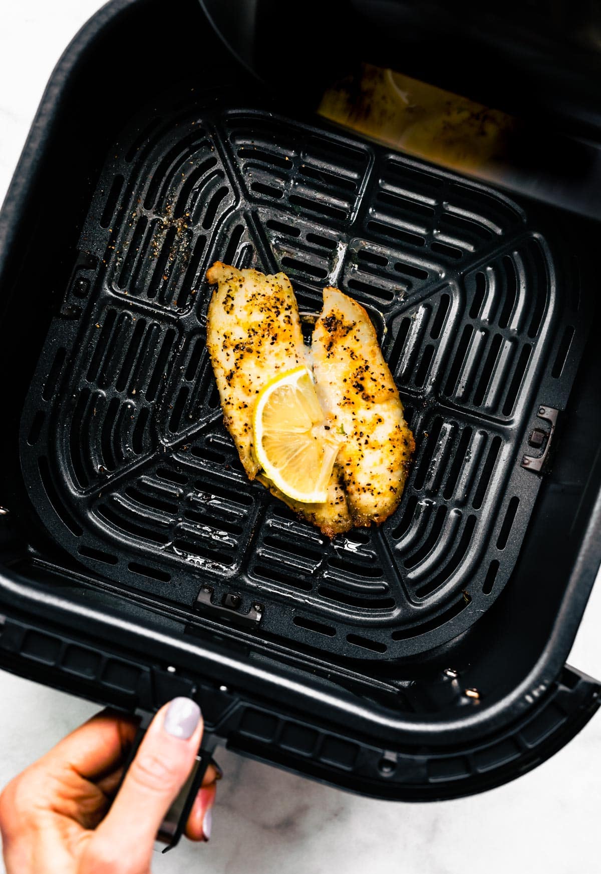 Overhead shot of a cooked tilapia fillet topped with a lemon in an air fryer