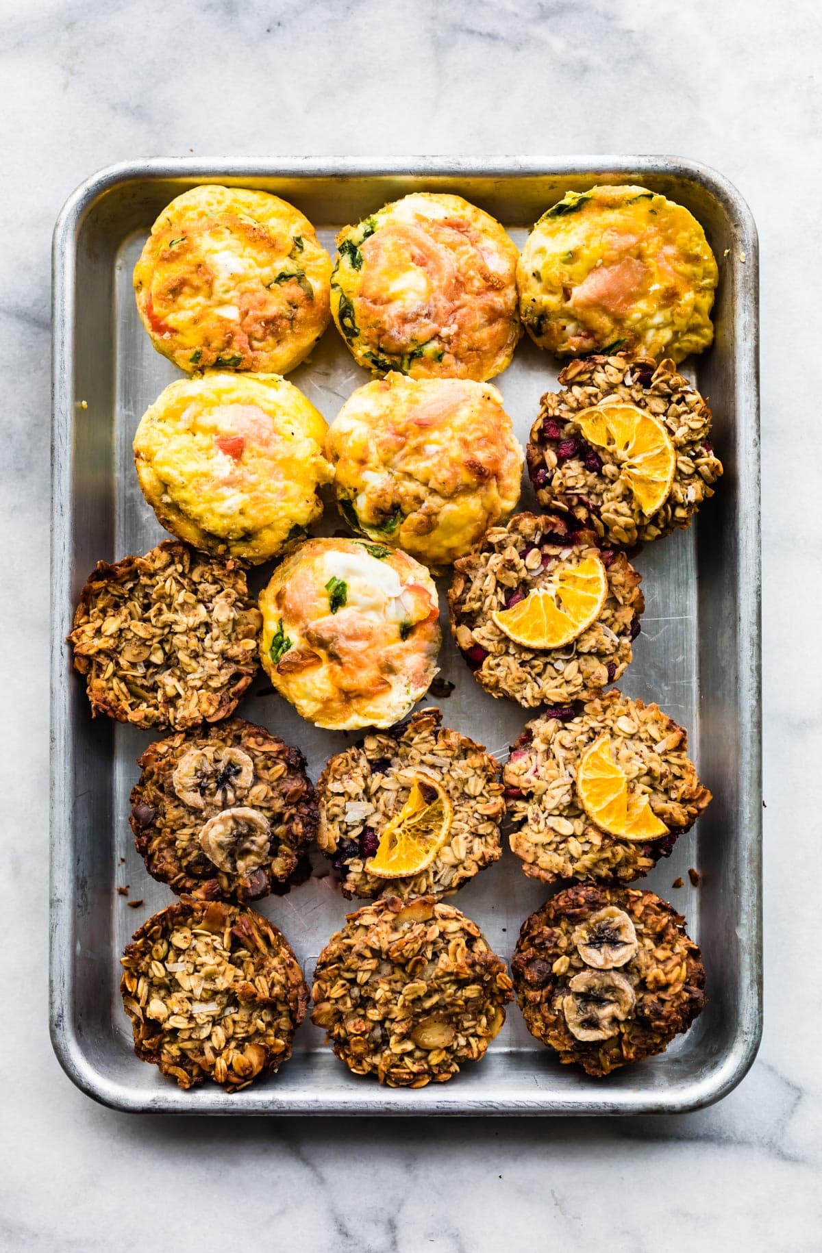 Overhead shot of frittata muffins and oatmeal cups on a sheet pan.