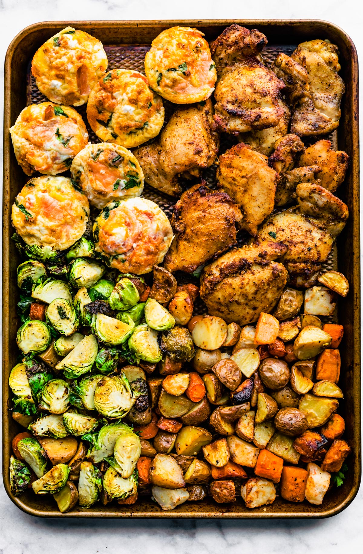 Overhead shot of frittata muffins, chicken, brussel sprouts and potatoes on a sheet pan.