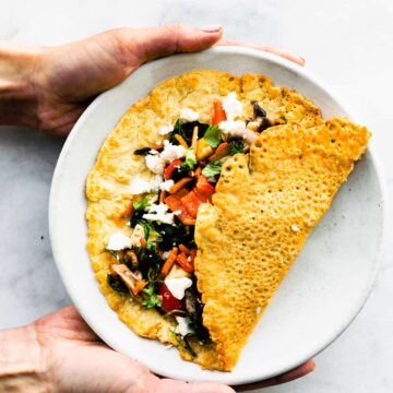Hands holding a Savory Chickpea Pancake on a plate.