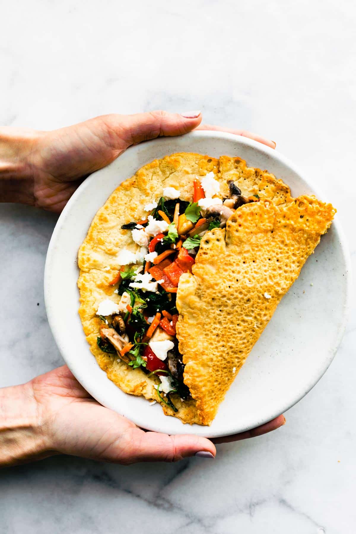 Hands holding a Savory Chickpea Pancake on a plate.