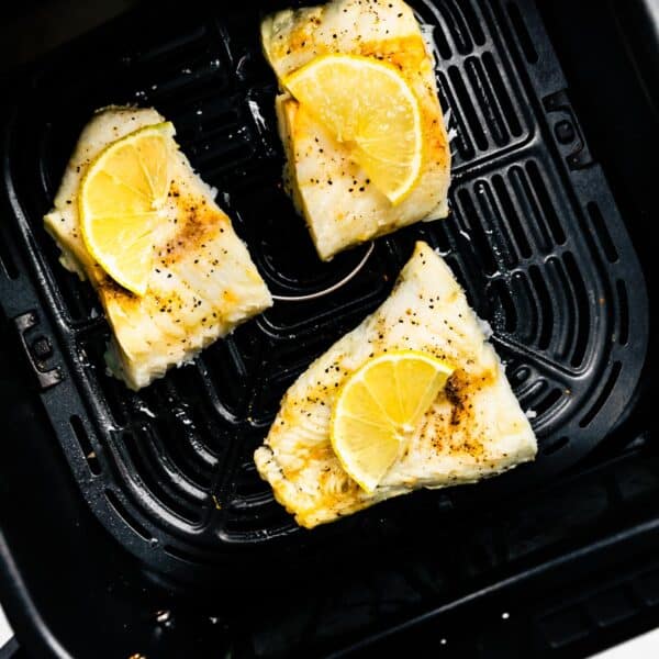 Three cooked fish filets topped with lemon in an air fryer