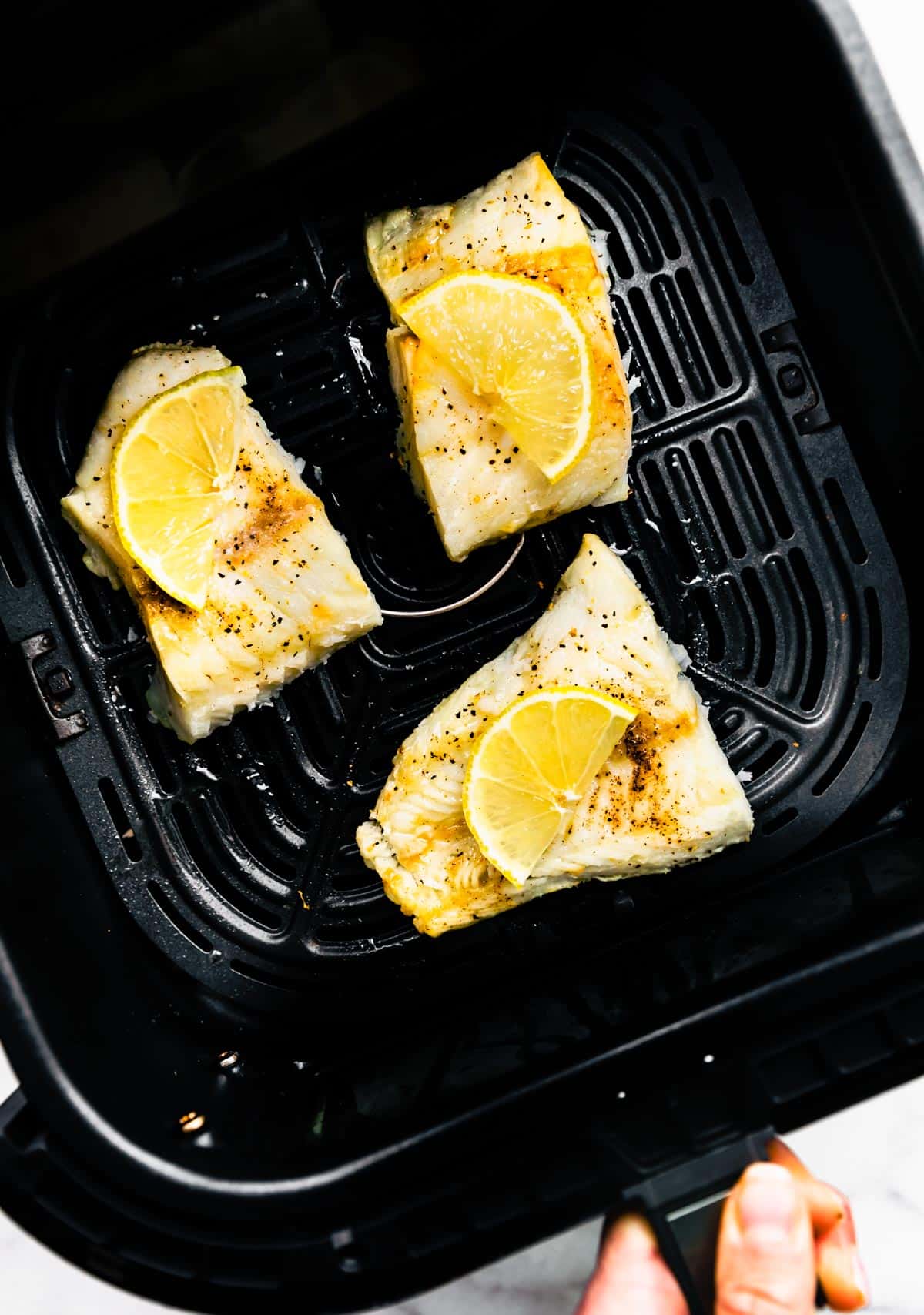 Three cooked fish fillets topped with lemon in an air fryer