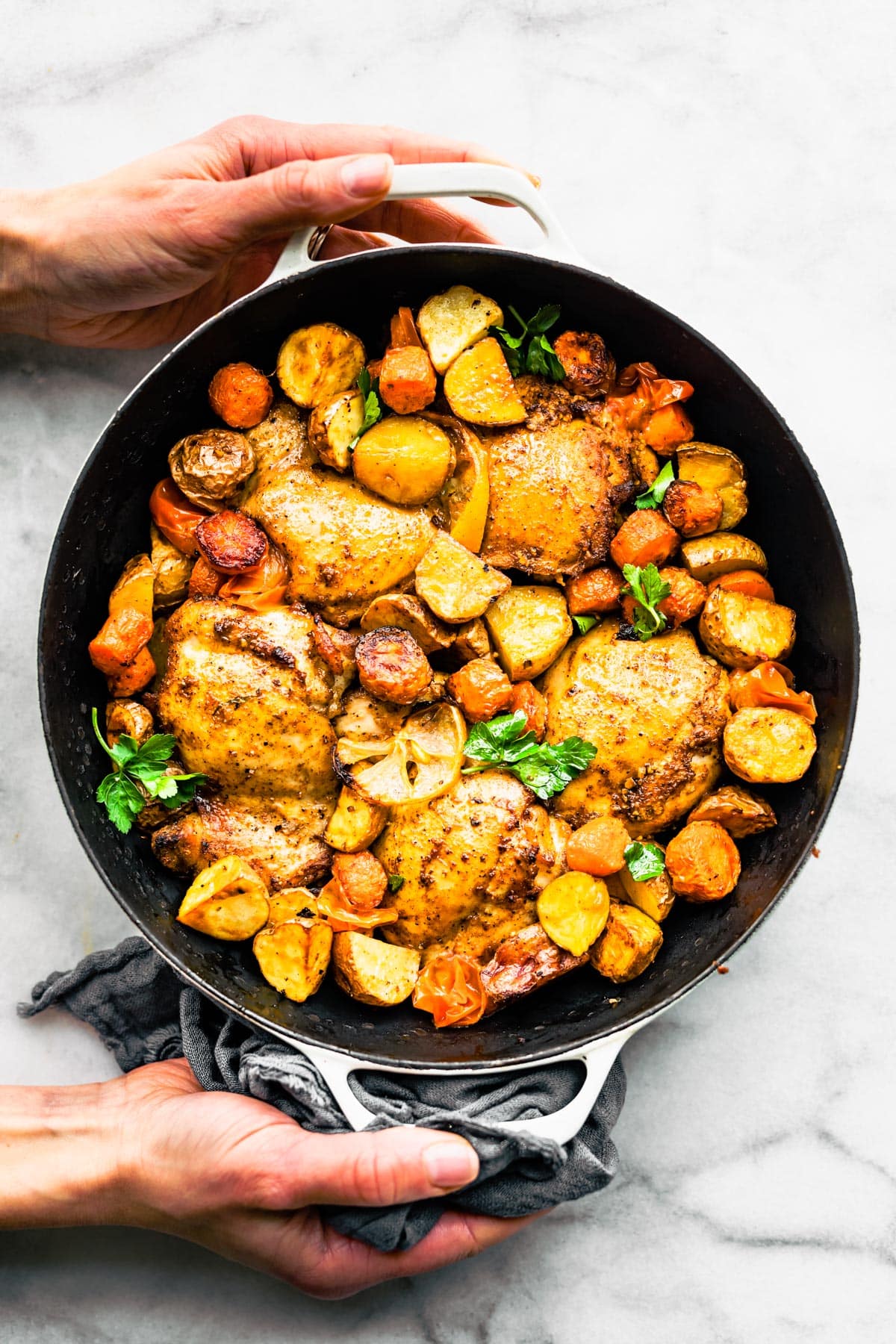 Overhead shot of Persian-Spiced Chicken and Potatoes in a pot with two hands holding pot.
