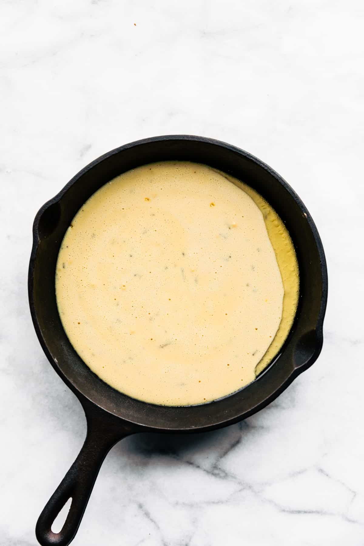 Uncooked socca batter and oil in cast iron pan