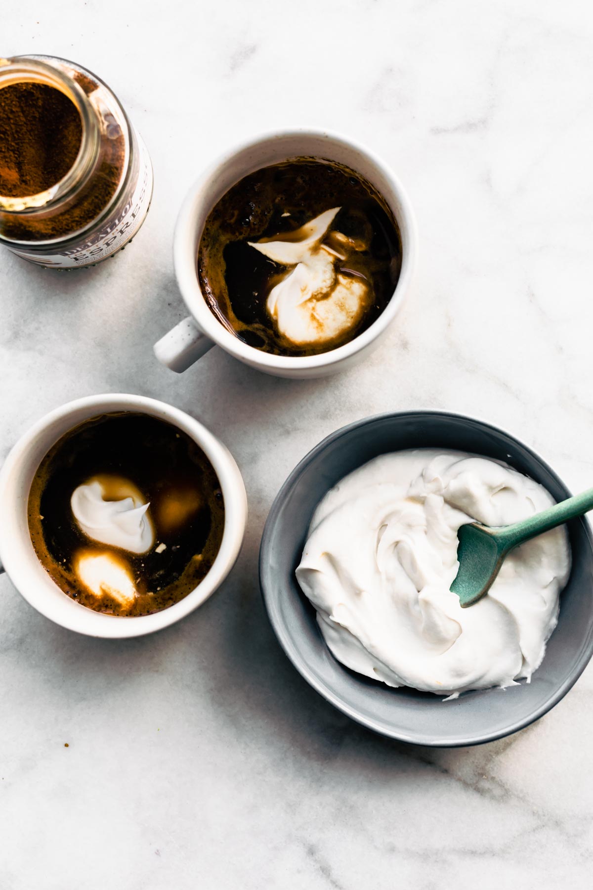 Two mugs of Espresso Con Panna with a bowl of whipped cream on a counter top.