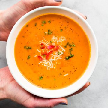 Hands holding a bowl of Roasted Red Pepper Soup.