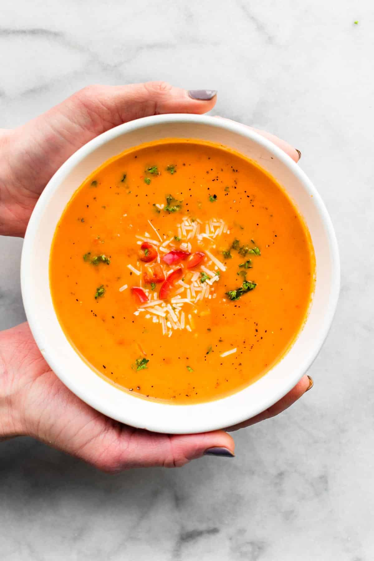 two hands holding a bowl of roasted red pepper soup