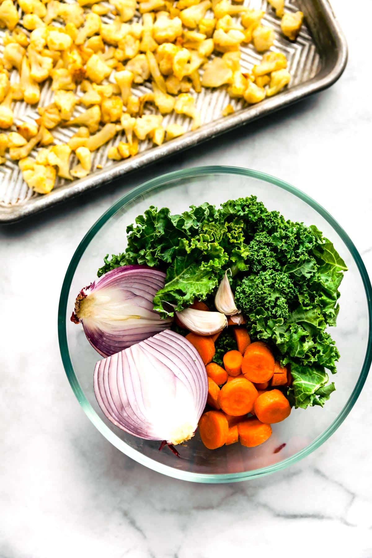 Red onion, carrots, garlic, and kale in a glass bowl together.