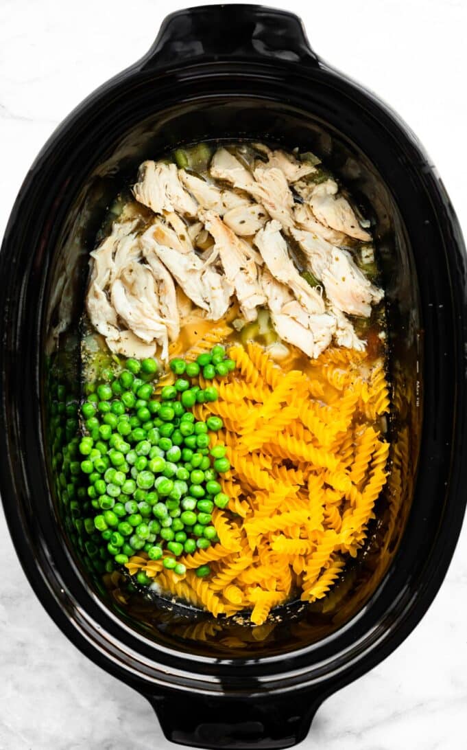 chicken pieces, gluten-free noodles, frozen peas, celery, carrots, onions, and broth in a slow cooker