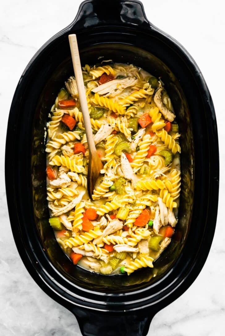 gluten-free chicken noodle soup in a slow cooker with a wooden spoon