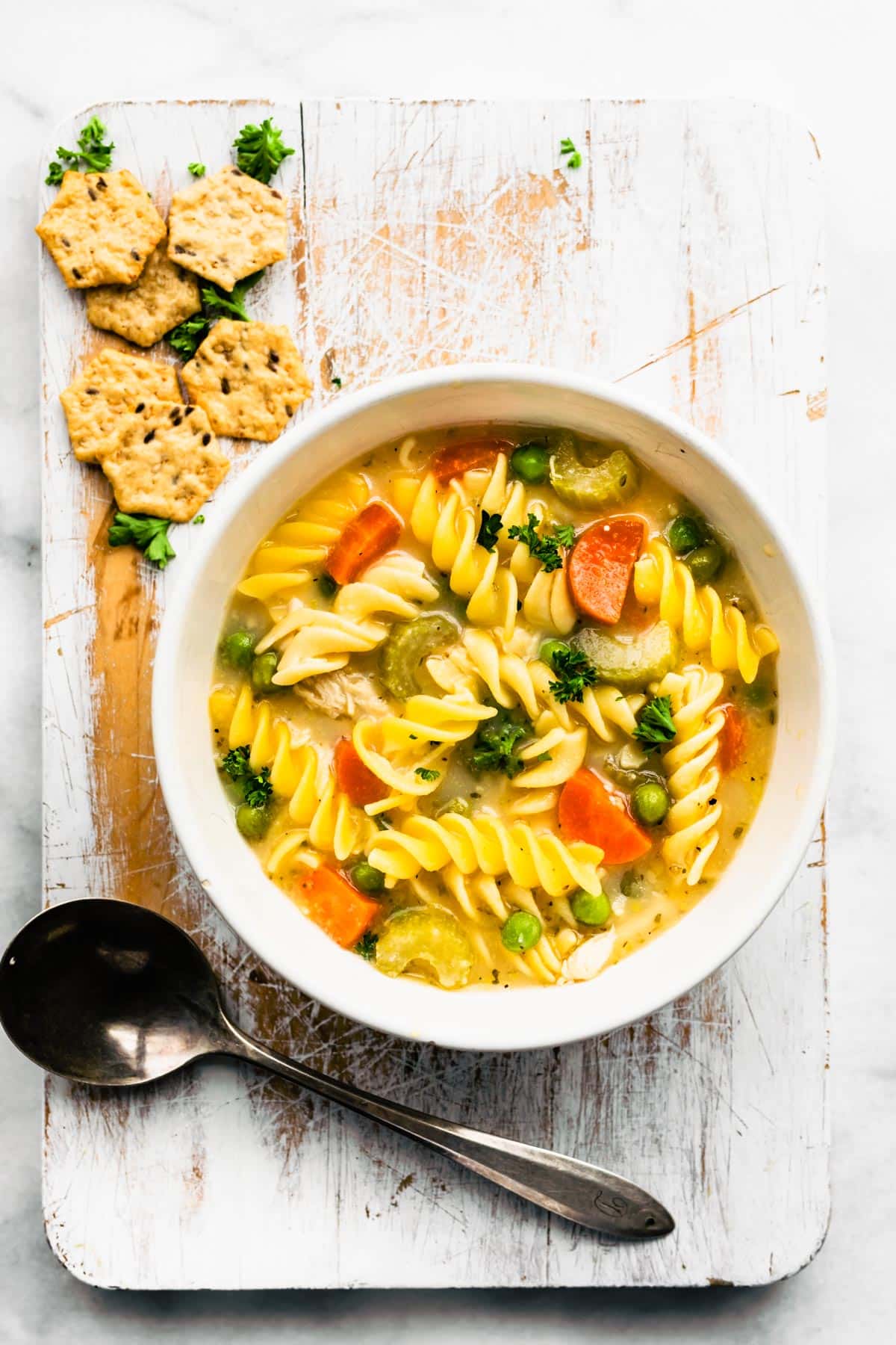 a bowl of gluten-free chicken noodle soup on a platter with a spoon and gluten-free crackers