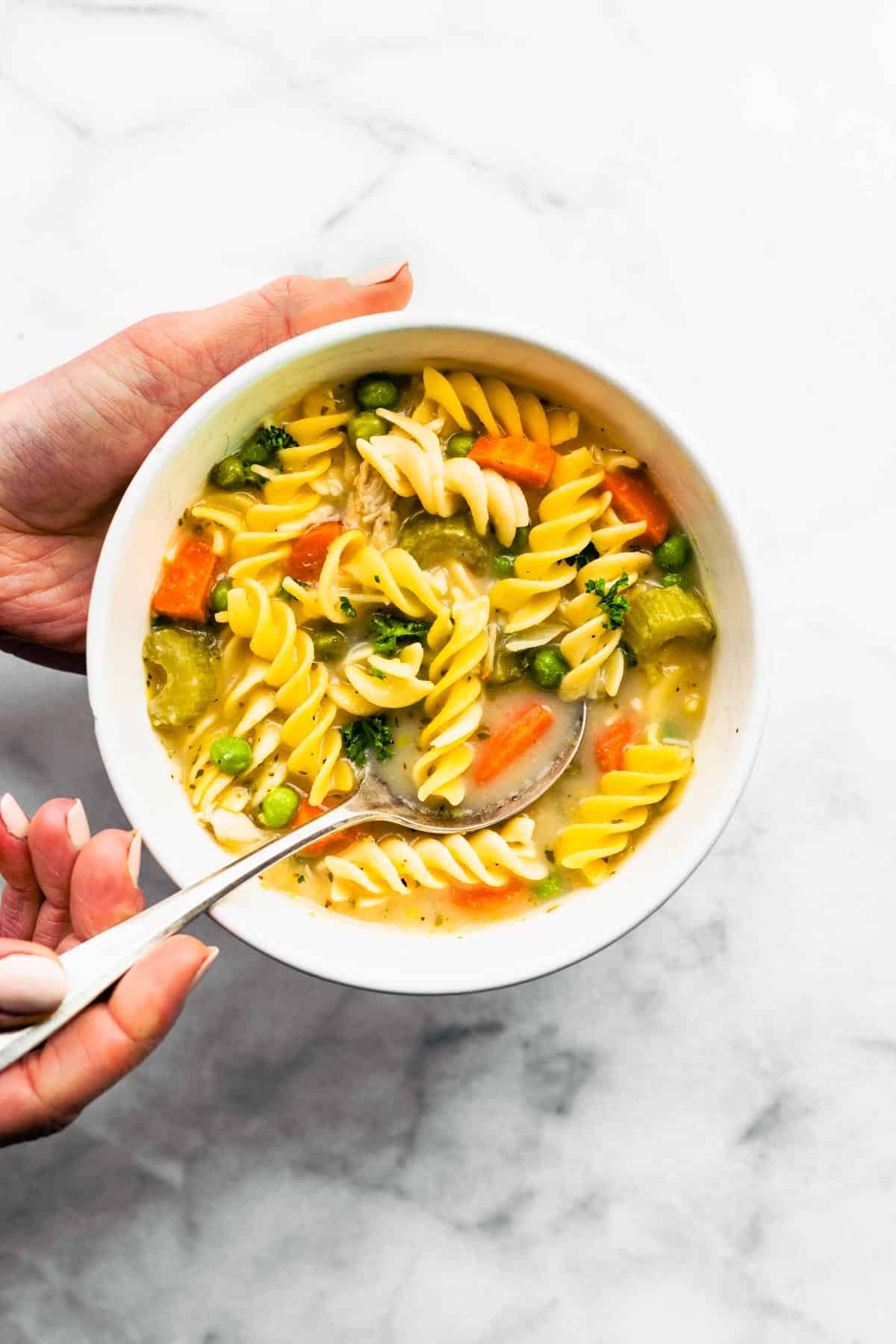 two hands holding a bowl of gluten-free chicken noodle soup and a spoon