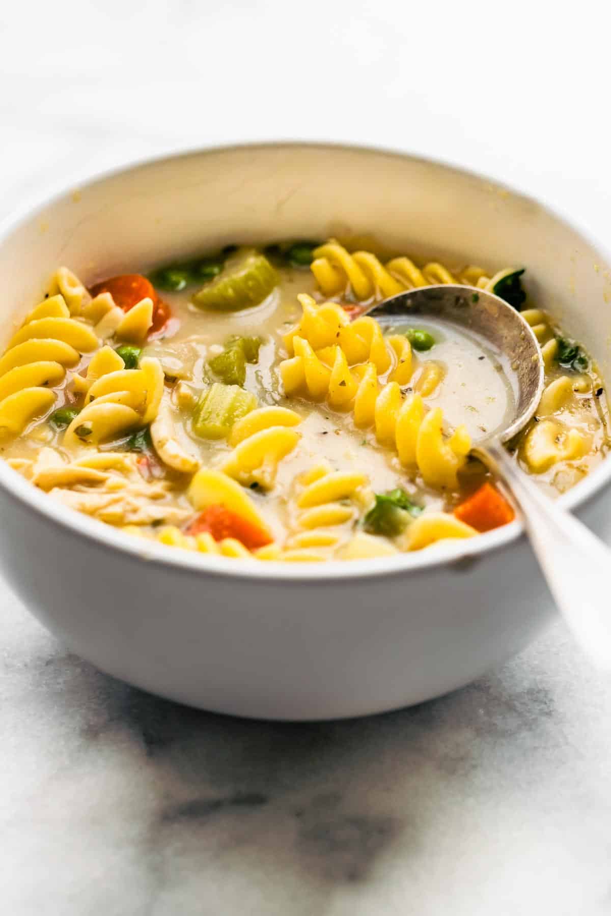 a bowl of gluten-free chicken noodle soup with a spoon sticking out