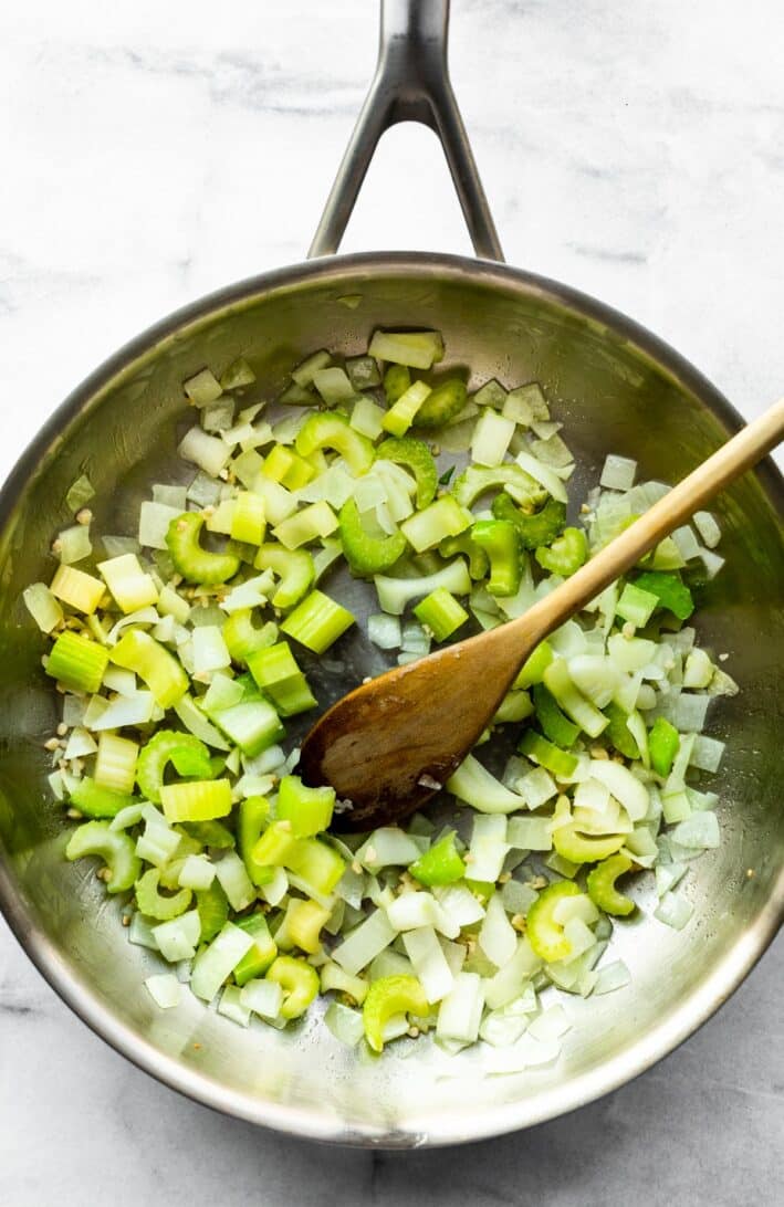 celery and onions in a skillet being stirred with a wooden spoon