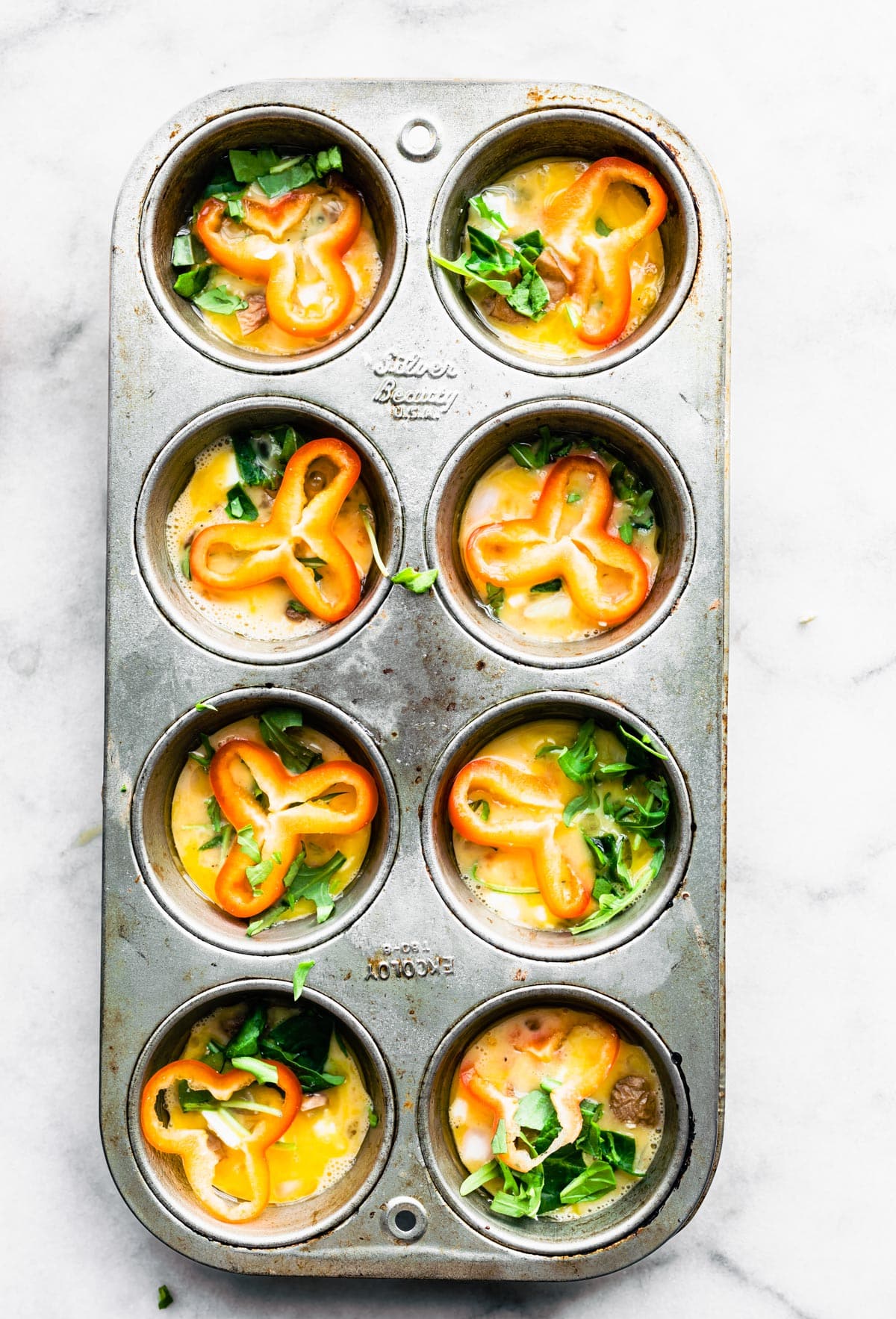 Egg base topped with veggie in a muffin pan.