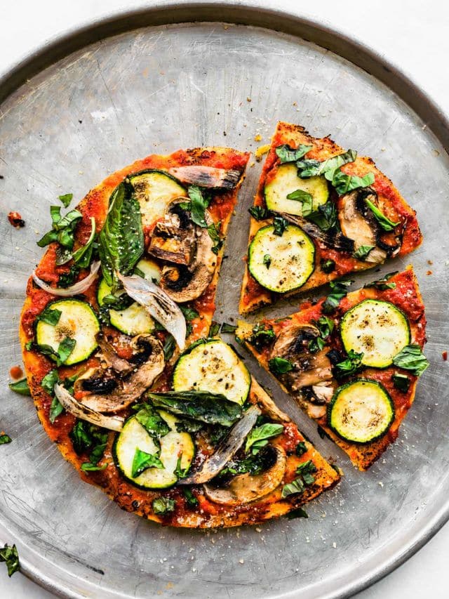 Overhead view socca pizza topped with zucchini, mushrooms, and basil on silver baking sheet.