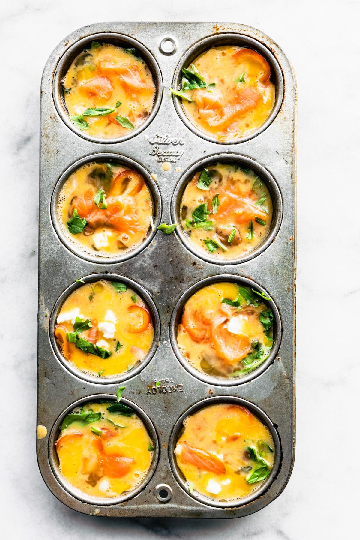 Egg base topped with veggie in a muffin pan and ready to go in the oven.