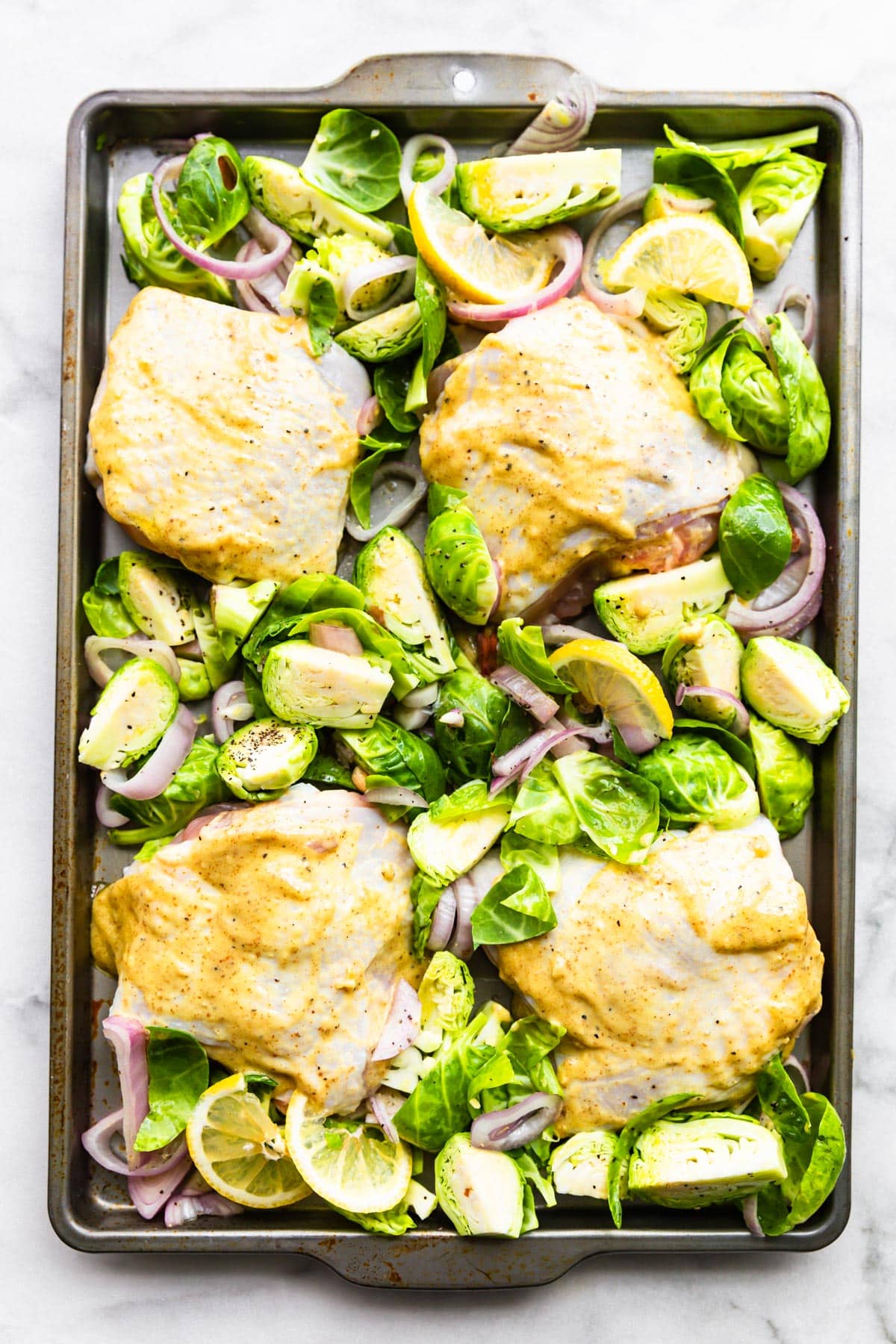 Overhead shot of Honey Mustard Chicken Thighs with Brussels Sprouts on a sheet pan prior to cooking.