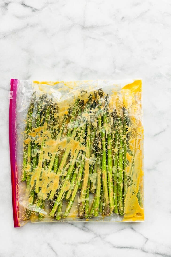 Asparagus spears in a sealable bag with seasonings and an egg wash.