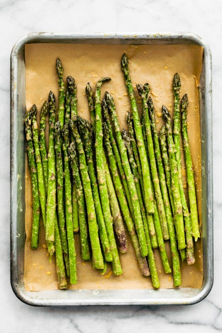 Asparagus spears in a baking dish on top of parchment paper.