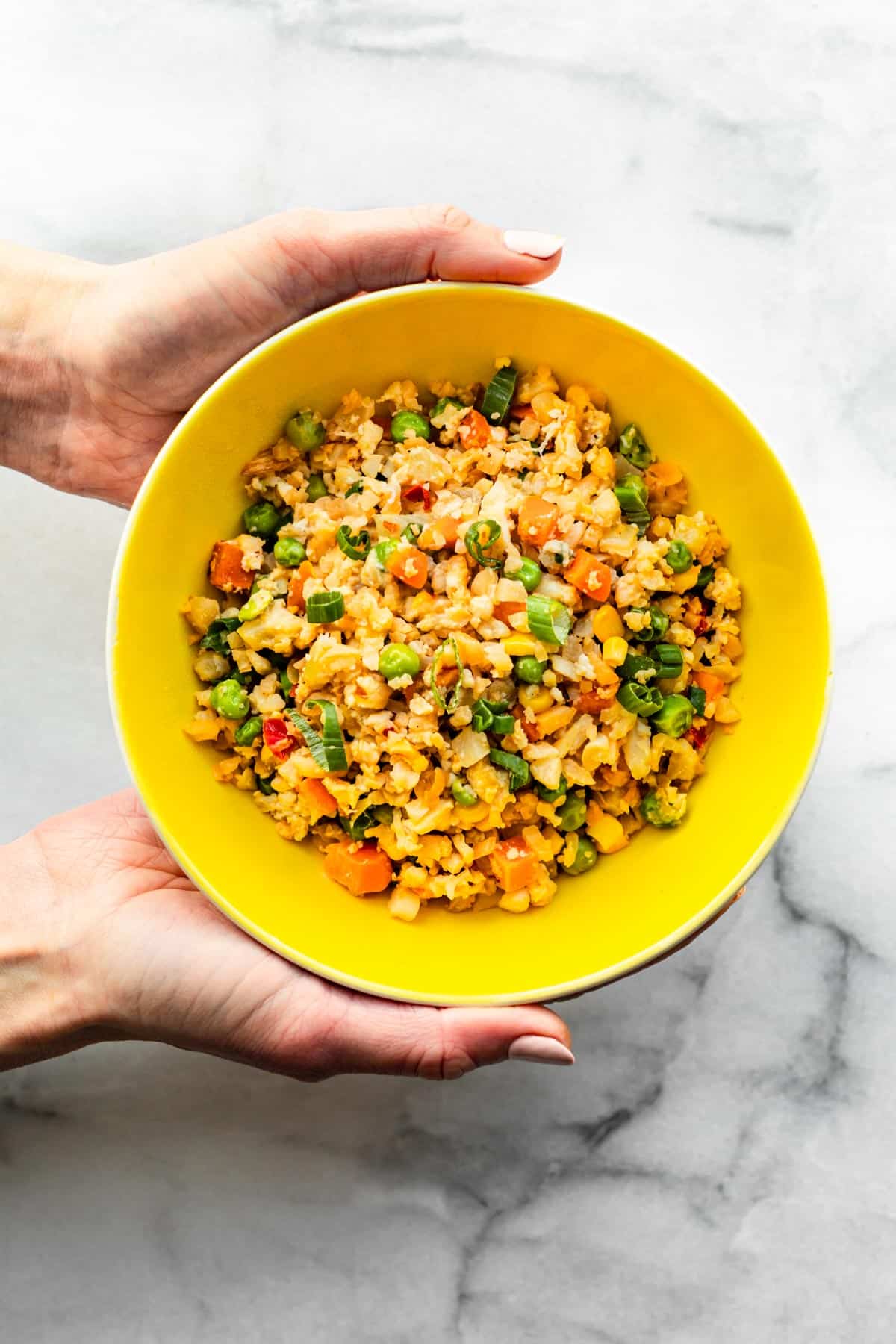 Hands holding a bowl of Cauliflower Fried Rice.