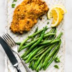 Gluten-Free Panko Chicken breast on a plate with green beans and a lemon wedge.