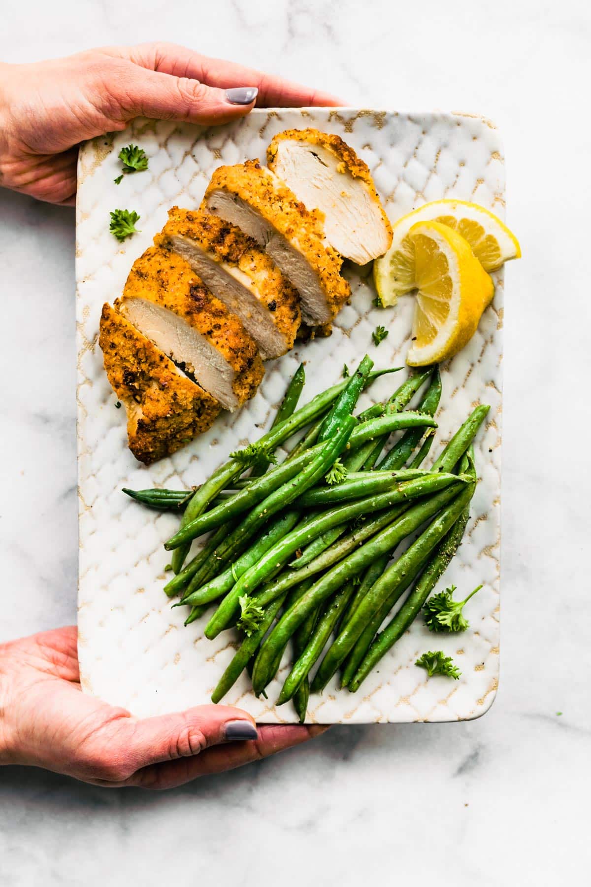 Sliced Gluten-Free Panko Chicken on a plate with green beans and a lemon wedge.