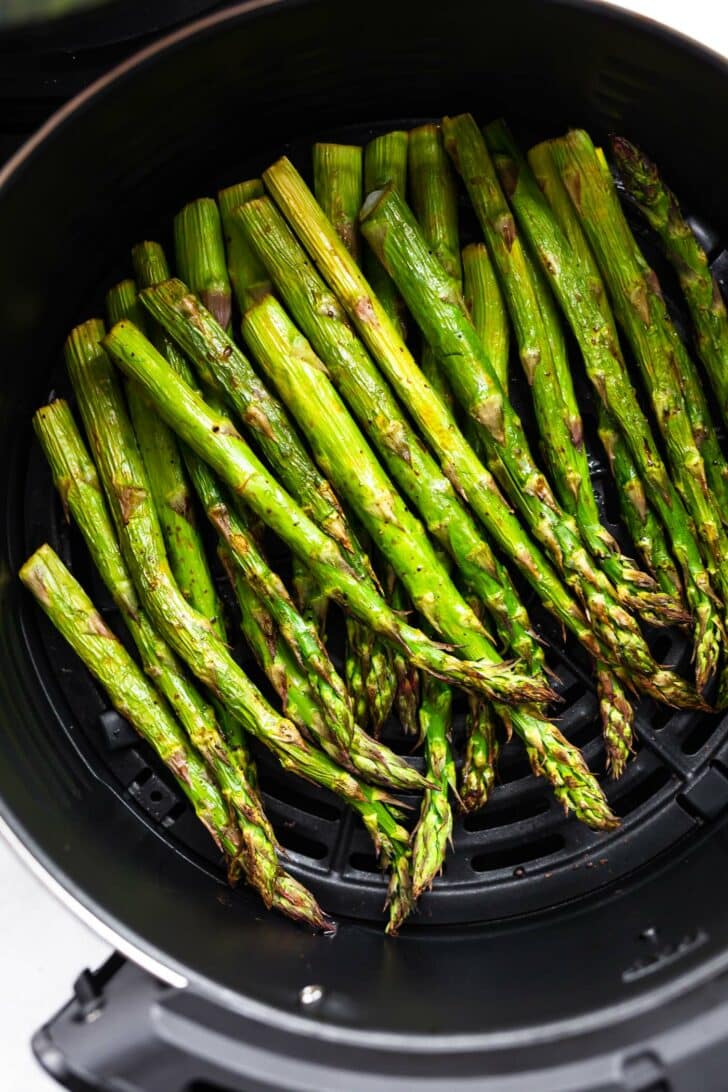 Air fried asparagus spears in an air fryer basket.