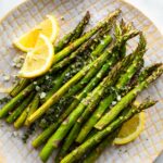 A plate full of air fried asparagus spears with lemon wedges on the side.