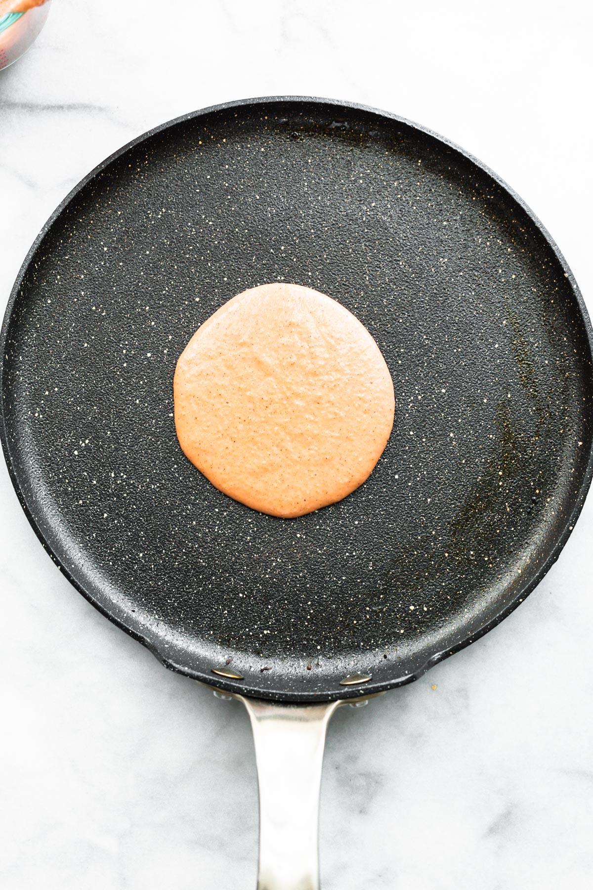 a circle of gluten-free carrot cake pancake batter cooking on a skillet