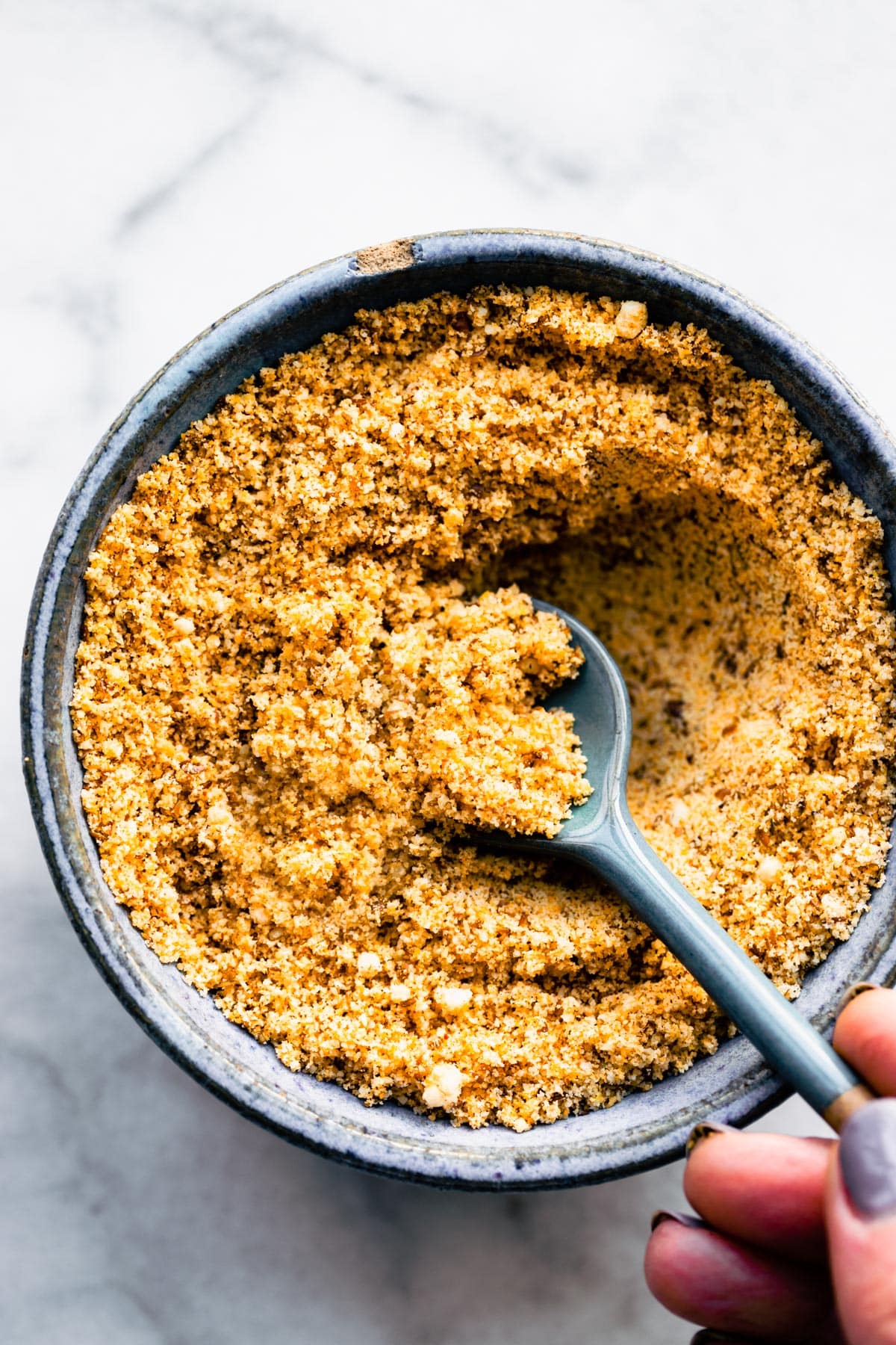 A bowl of gluten-free panko breadcrumbs with a spoon sticking out.