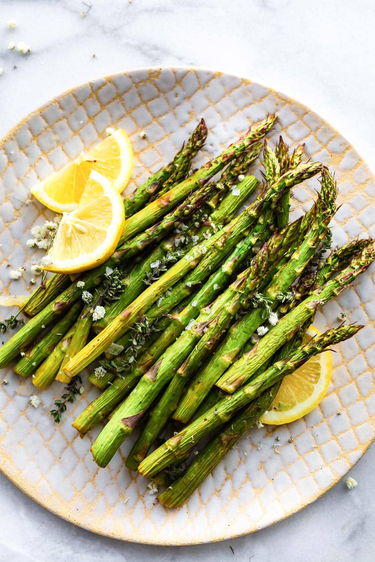 A plate full of air fried asparagus spears with lemon wedges on the side.
