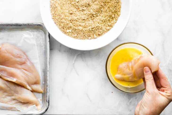 Gluten-Free Panko Chicken breast being dipped in whisked egg mixture.